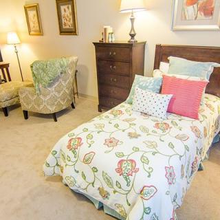 A cozy bedroom with a single bed adorned with floral bedding, complemented by a comfortable chair and decorative elements.