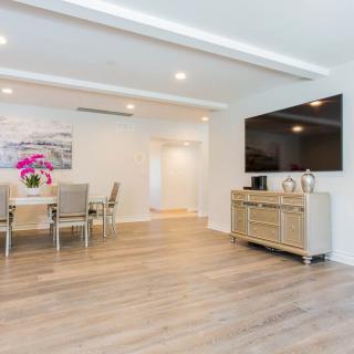 A modern, minimalist living and dining space featuring a large TV, sleek furniture, and hardwood floors.