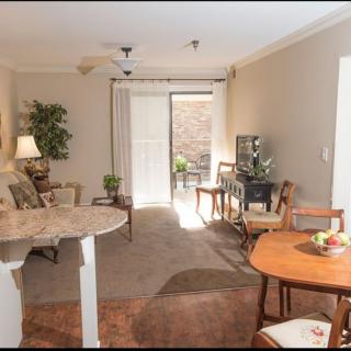 A cozy living and dining area with natural light, featuring comfortable seating, a TV, and stylish decor.