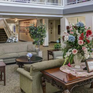A cozy lobby area featuring comfortable seating, a large floral arrangement on a table, and an elegant staircase.