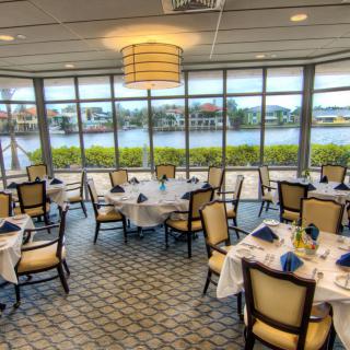 An elegant dining room with neatly arranged tables and chairs, offering a scenic view through large windows.