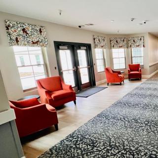 A cozy lobby area featuring vibrant red chairs, large windows with patterned curtains, and a textured carpet.