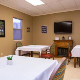 A small dining area with tables covered in white tablecloths, decorated with artwork and a wall-mounted television.