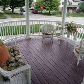 A cozy porch with wicker furniture and a curved railing overlooking a suburban street.