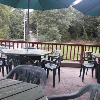 A view of an outdoor dining area with tables and chairs under green umbrellas, surrounded by nature.