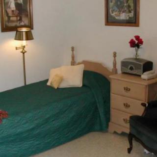 A cozy bedroom featuring a single bed with green bedding, a nightstand with a vintage radio, and decorative paintings on the wall.