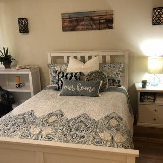 A cozy bedroom with a neatly made bed, featuring decorative pillows and a patterned quilt, accompanied by a lamp on the nightstand.