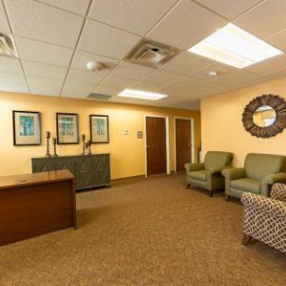 A cozy and inviting waiting room featuring comfortable green chairs, decorative artwork, and a welcoming reception area.