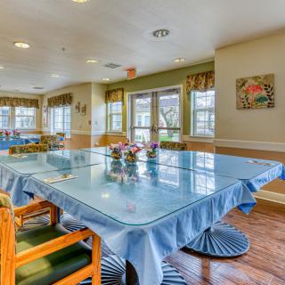 A well-lit dining area with tables and chairs, accented by natural light from large windows and simple decor.