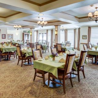 Spacious dining room with elegantly set tables and chairs, featuring chandeliers and large windows.