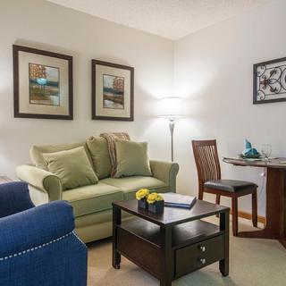 A cozy living room with a green sofa, blue armchair, and wall art.