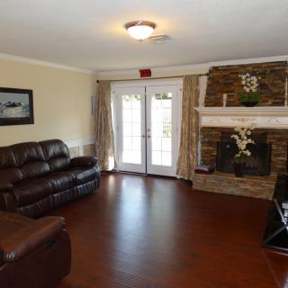 A cozy living room featuring a leather sofa, stone fireplace, and hardwood flooring with natural light from French doors.