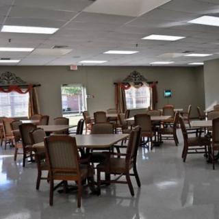 An empty indoor dining area with multiple tables and chairs, illuminated by ceiling lights.