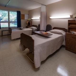 A patient room in a hospital featuring two beds and natural lighting.