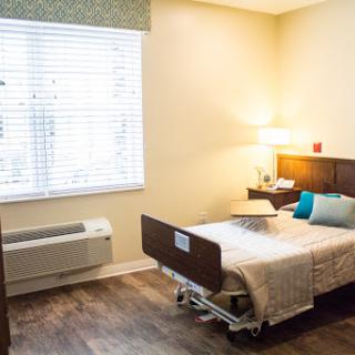 A well-lit hospital patient room featuring a bed, bedside lamp, and window.