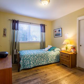 A cozy bedroom with a bed, wooden flooring, and a warm light from a lamp.