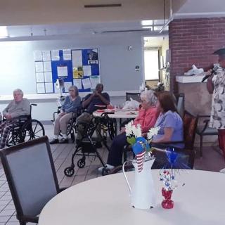 A group of elderly individuals sitting in a community room, some in wheelchairs, engaged in social activities.