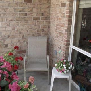 A cozy patio with a chair, vibrant flowers, and a brick wall backdrop.
