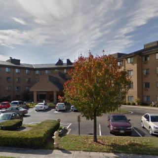 A residential apartment building with a parking lot and trees in front.