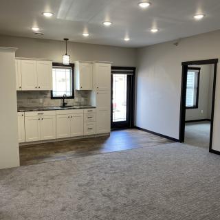 A modern apartment interior with an open kitchen and living area, featuring minimalist design and ample lighting.