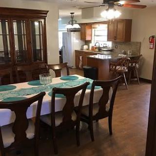 An open dining area leading into a kitchen with wooden furniture and flooring.