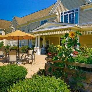 A beautiful garden patio with outdoor furniture and a sunflower, set against a charming residential building on a sunny day.