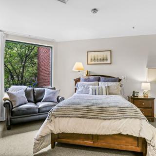 A cozy bedroom with a double bed, sofa, and a large window providing natural light.