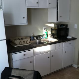 A small kitchen with white cabinets, a countertop, and a dish drainer by the sink.