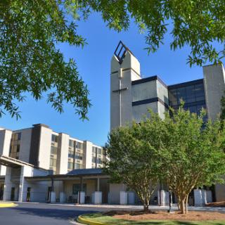 A modern hospital building surrounded by lush greenery and clear blue skies.