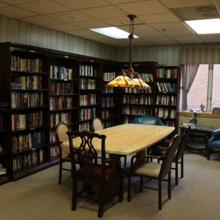 A cozy library room with a table surrounded by chairs and bookshelves lining the walls.