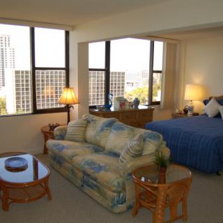 A cozy apartment featuring a bedroom and living area with large windows offering a city view.