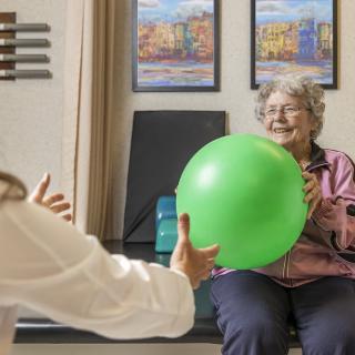 An elderly woman engaging in a physical therapy session with a green exercise ball.
