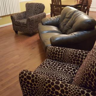 A stylish living room featuring a black leather sofa and leopard print armchairs on a wooden floor.