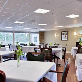 A spacious and well-lit dining area featuring elegantly set tables with white tablecloths and floral centerpieces.