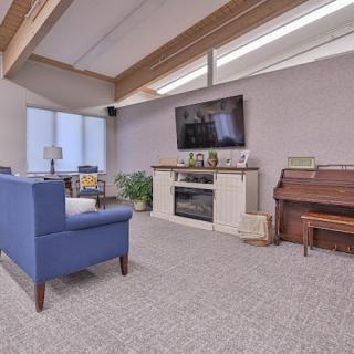A cozy living room featuring a blue sofa, piano, and a television mounted above a fireplace.