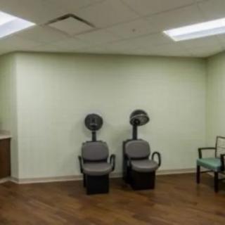 An empty salon room with two hair dryer chairs and wooden flooring.