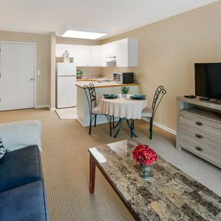 A cozy living area with an open-plan kitchen, featuring a television, sofa, and dining table.