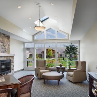 A modern and cozy living room with large windows, a skylight, and comfortable seating around a fireplace.