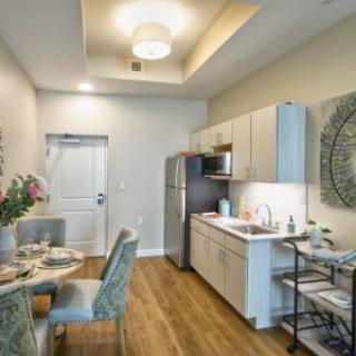 A modern apartment kitchen and dining area with sleek furnishings and wooden flooring.