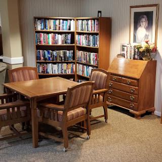 A cozy reading nook with a wooden table and chairs beside a bookshelf filled with books.