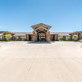 A wide view of a brick building with a prominent entrance and a large driveway on a clear, sunny day.