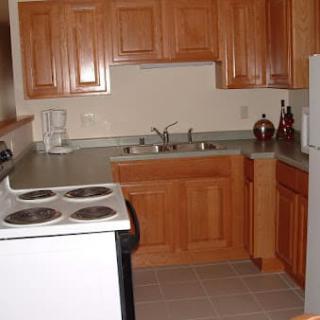 A small kitchen with wooden cabinets, a stove, sink, and refrigerator.