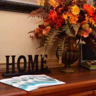 A cozy home setup featuring a decorative vase with autumn flowers and a 'HOME' sign on a wooden table.