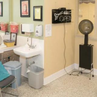 A cozy salon interior featuring a hair dryer, sink, and seating area with wall decorations.
