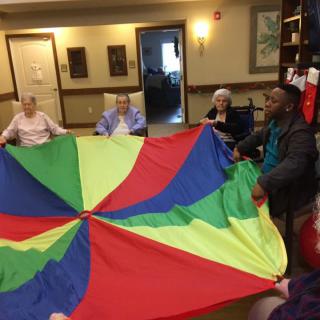 A group of elderly individuals participating in a colorful parachute activity at a community center.