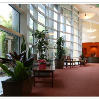 A spacious and well-lit lobby area with large windows, plants, and comfortable seating.