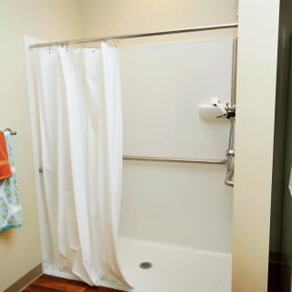A bathroom featuring a shower with a white curtain and towels hanging on the wall.