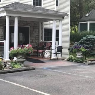 A building entrance with a covered porch, featuring chairs, plants, and flowers.
