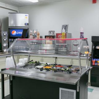 A view of a food service area featuring a counter with condiment options and beverage dispensers.