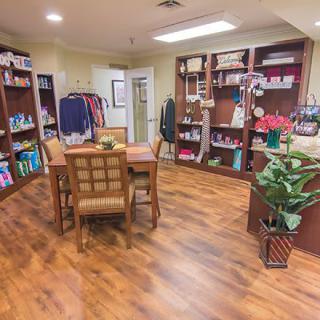 A cozy store interior with wooden flooring, a central table surrounded by chairs, and shelves filled with various items.